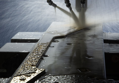 Machine cutting metal with water spray, industrial manufacturing process.